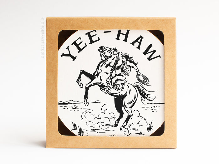 The Yeehaw Cowgirl Coaster Set by Onderkast Studio comes in a square window box featuring a cowgirl on a rearing horse with YEE-HAW above—a fun way to showcase these handmade letterpress coasters.